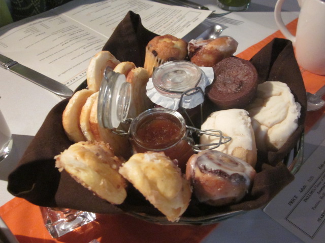 Bread basket full of mini cinnamon rolls, palmiers, muffins, breads, and fruit preserves